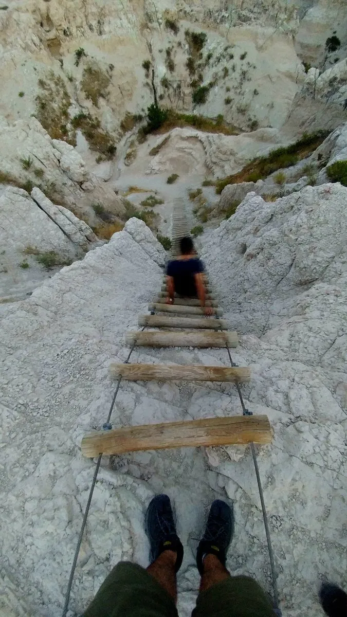 Looking down a wooden ladder bolted to a steep white rock face in the Badlands, with a hiker partway down