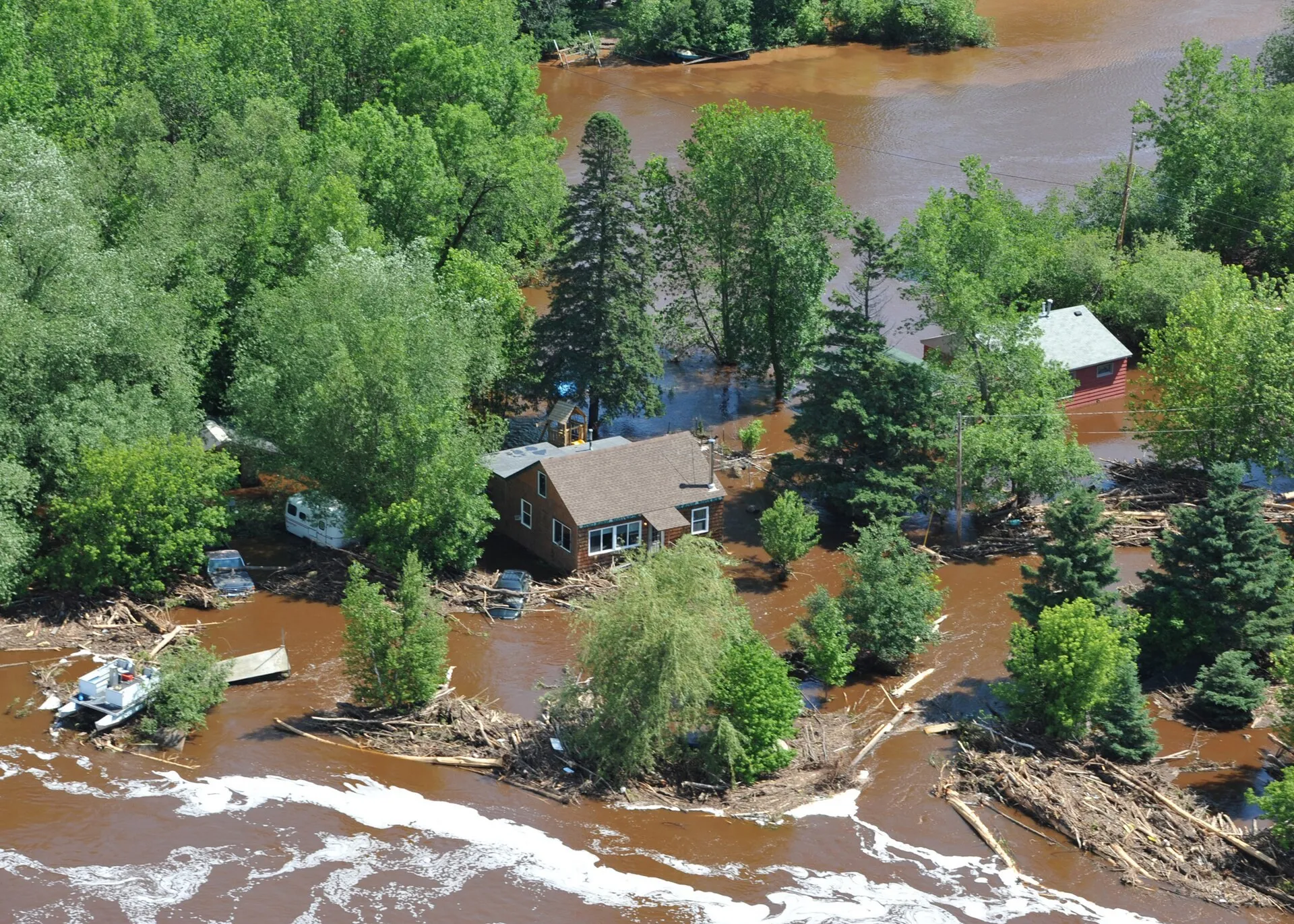 Aerial view of houses and trees surrounded by brown floodwater near Duluth