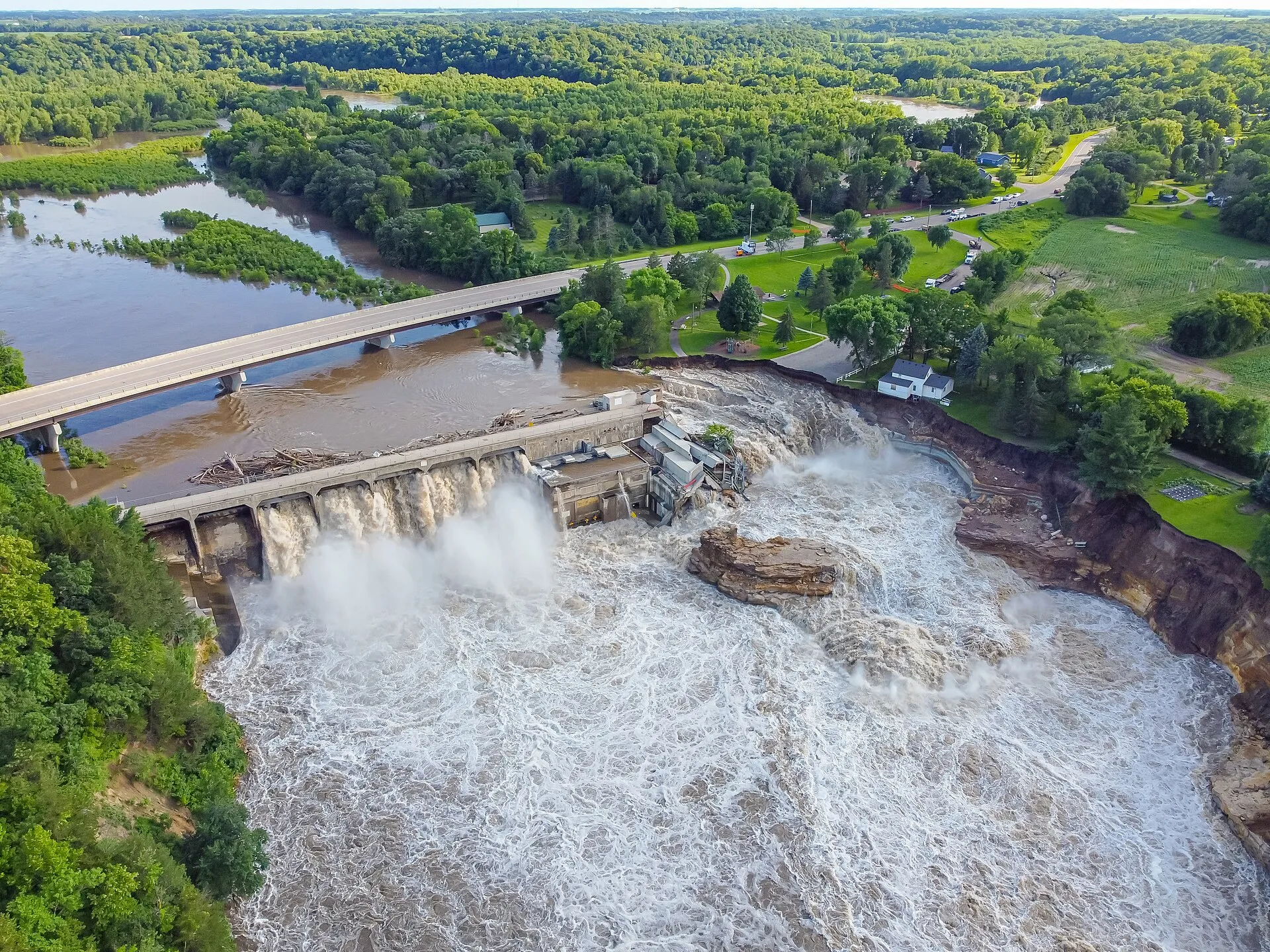 Aerial view of the Blue Earth River pouring around the west end of the Rapidan Dam, with the eroded bank beside it